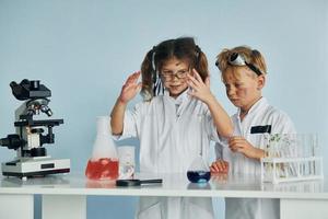 menina e menino em casacos brancos interpretam cientistas em laboratório usando equipamentos foto