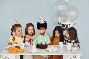 senta-se à mesa. as crianças comemorando a festa de aniversário dentro de casa se divertem juntas foto