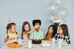 senta-se à mesa. as crianças comemorando a festa de aniversário dentro de casa se divertem juntas foto