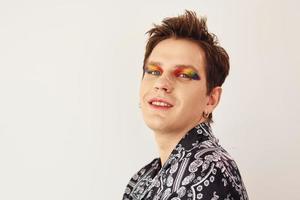 jovem gay está de pé no estúdio e posando para uma câmera. maquiagem multicolorida nos dedos do rosto foto