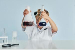 menino de casaco jogando um cientista no laboratório usando equipamentos foto