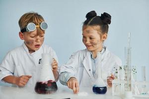 menino trabalha com líquido em tubos de ensaio. crianças em jalecos brancos interpretam cientistas em laboratório usando equipamentos foto