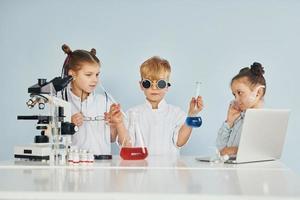 de pé ao lado da mesa com tubos de ensaio. crianças em jalecos brancos interpretam cientistas em laboratório usando equipamentos foto