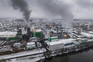 vista aérea panorâmica de inverno de fumaça escura de tubos de empresa de carpintaria com neve. conceito de poluição do ar e da água. foto