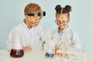 menina com menino trabalhando juntos. crianças em jalecos brancos interpretam cientistas em laboratório usando equipamentos foto