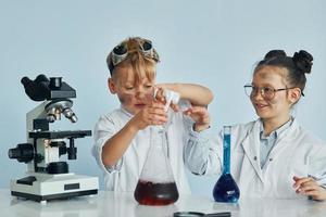 menina e menino em casacos brancos interpretam cientistas em laboratório usando equipamentos foto