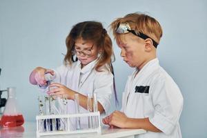 menina e menino em casacos brancos interpretam cientistas em laboratório usando equipamentos foto