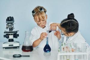 menina e menino em casacos brancos interpretam cientistas em laboratório usando equipamentos foto