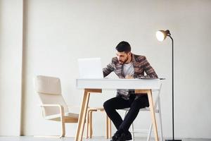 senta-se à mesa no escritório. jovem empresário elegante terno dentro de casa. concepção de sucesso foto