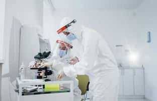 usando microscópio. trabalhadoras médicas em uniforme de proteção trabalham na vacina covid-19 foto