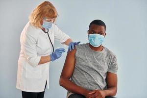 médico sênior dando injeção para jovem afro-americano no hospital foto