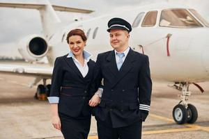 homem com mulher. tripulação de aeronave em uniforme de trabalho está junto ao ar livre perto de avião foto