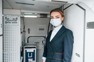 em luvas de proteção e máscara. jovem aeromoça no trabalho no avião de passageiros foto