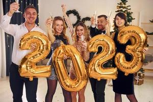 2023 balões nas mãos. grupo de pessoas tem uma festa de ano novo dentro de casa juntos foto