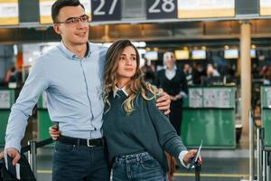 abraçando um ao outro. jovem casal está no aeroporto juntos foto