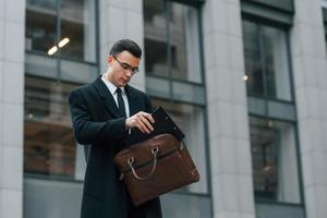 com bolsa marrom. empresário de terno preto e gravata está ao ar livre na cidade foto