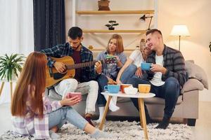 tocando violão. grupo de amigos tem festa dentro de casa juntos foto