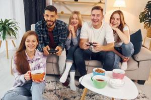 usando joysticks para jogar videogame. grupo de amigos tem festa dentro de casa juntos foto