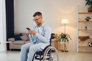 usando telefone. homem com deficiência em cadeira de rodas está em casa foto