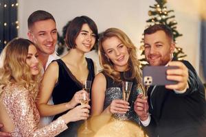fazendo selfie. grupo de pessoas tem uma festa de ano novo dentro de casa juntos foto
