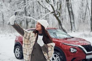 natureza bela. jovem está ao ar livre perto de seu automóvel vermelho no inverno foto