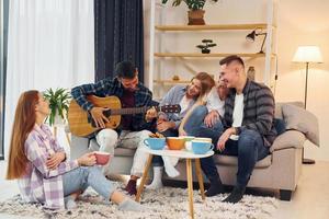 tocando violão. grupo de amigos tem festa dentro de casa juntos foto