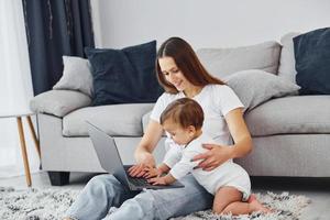 assistindo no laptop. mãe com sua filha está dentro de casa juntos foto