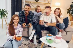 usando joysticks para jogar videogame. grupo de amigos tem festa dentro de casa juntos foto