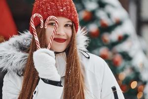 segurando doces. mulher jovem feliz em pé ao ar livre e comemorando as férias de natal foto