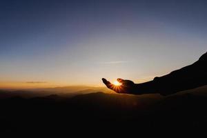 silhueta do homem levanta a mão rezando no topo da montanha e do céu pôr do sol abstrato. liberdade e conceito de aventura de viagem. foto