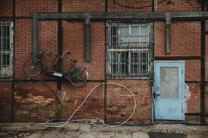 porta azul na parede de tijolo vermelho do edifício em enxaimel com bicicleta em tandem pendurada na parede nas docas de gdansk foto