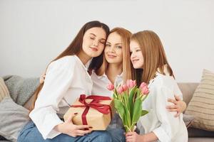 fazendo surpresa com flores. jovem mãe com suas duas filhas em casa durante o dia foto