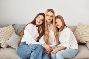 sentado no sofá. jovem mãe com suas duas filhas em casa durante o dia foto