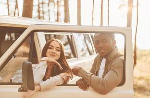 perto do ônibus branco. jovem casal está viajando na floresta durante o dia juntos foto