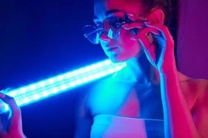 segura bastão de iluminação neon. jovem elegante em pé no estúdio foto