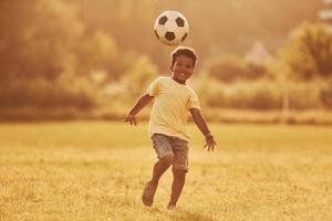 joga futebol. garoto afro-americano divirta-se no campo durante o dia de verão foto