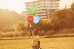 com balões nas mãos. garoto afro-americano divirta-se no campo durante o dia de verão foto