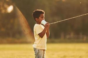 falando usando copo no nó. garoto afro-americano divirta-se no campo durante o dia de verão foto