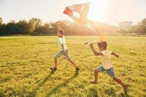 correndo com pipa. duas crianças afro-americanas se divertem no campo durante o dia de verão juntos foto