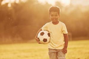 jovem jogador de futebol. garoto afro-americano divirta-se no campo durante o dia de verão foto