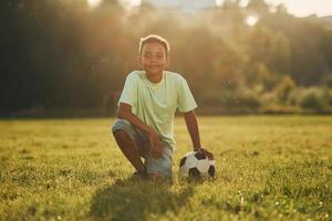 Tire uma folga. com bola de futebol. garoto afro-americano divirta-se no campo durante o dia de verão foto