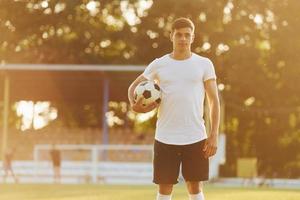 de pé e posando. jovem jogador de futebol tem treinamento no campo esportivo foto