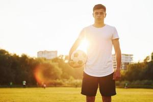 de pé e segurando a bola na mão. jovem jogador de futebol tem treinamento no campo esportivo foto