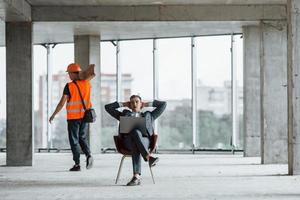 objeto em movimento. homem de terno e faz-tudo em roupas de proteção laranja está trabalhando na construção foto