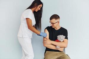 homem segurando ursinho de pelúcia durante o procedimento. médico de uniforme fazendo vacinação para o paciente foto