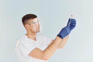 de uniforme branco. jovem médico masculino está dentro de casa contra fundo branco foto