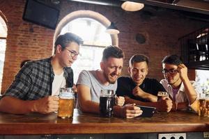 vista lateral de amigos com cerveja. pessoas em roupas casuais sentadas no pub foto