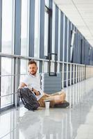 homem sentado no chão. jovem viajante está no hall de entrada do aeroporto foto