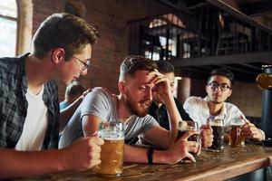 vista lateral de amigos com cerveja. pessoas em roupas casuais sentadas no pub foto