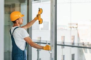 limpando janelas. jovem trabalhando de uniforme na construção durante o dia foto